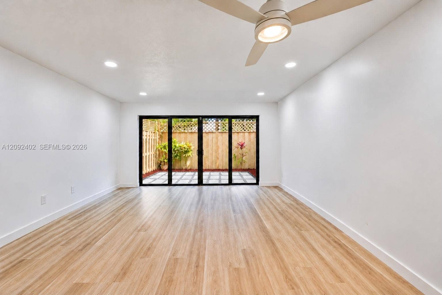 499 SE 13th Street, #7E, Fort Lauderdale, FL 33316 Interior space featuring wood-finish flooring, recessed lighting, and a modern ceiling fan, highlighted by a multi-panel glass door system opening to a private patio with wood fencing