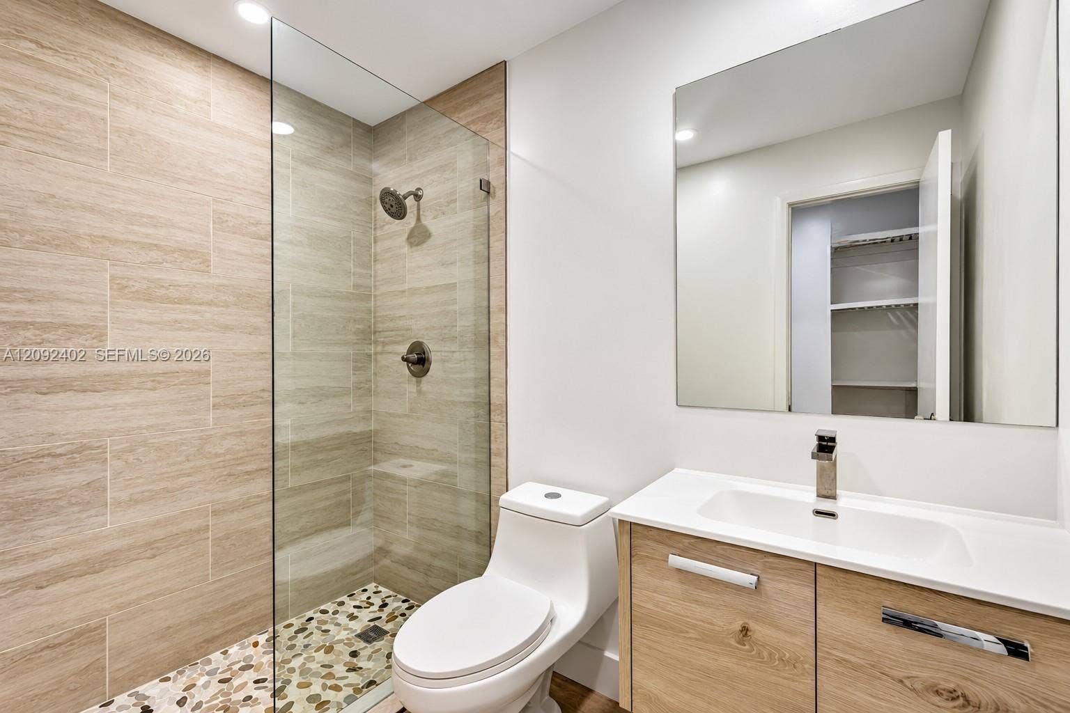 499 SE 13th Street, #7E, Fort Lauderdale, FL 33316 Bathroom featuring a glass-enclosed shower with pebble-stone flooring and large-format wall tile, wood-finish vanity, solid-surface countertop with integrated sink, and polished chrome fixtures