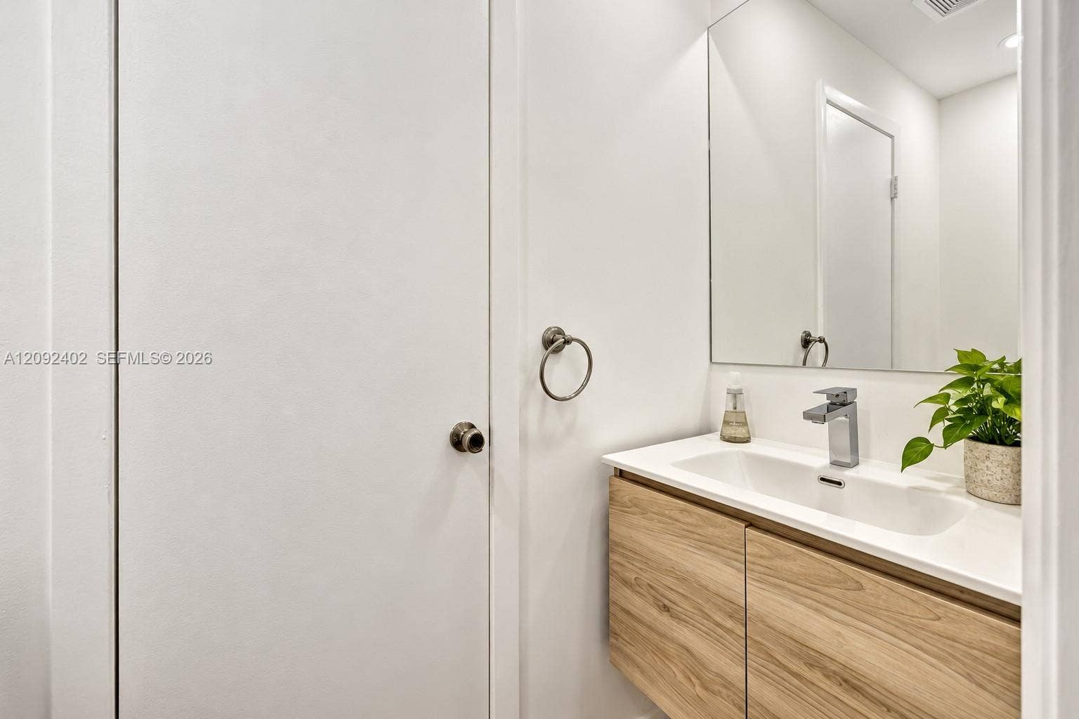 499 SE 13th Street, #7E, Fort Lauderdale, FL 33316 Floating vanity with wood-finish cabinetry, white countertop, integrated rectangular sink, chrome single-handle faucet, and wall-mounted mirror