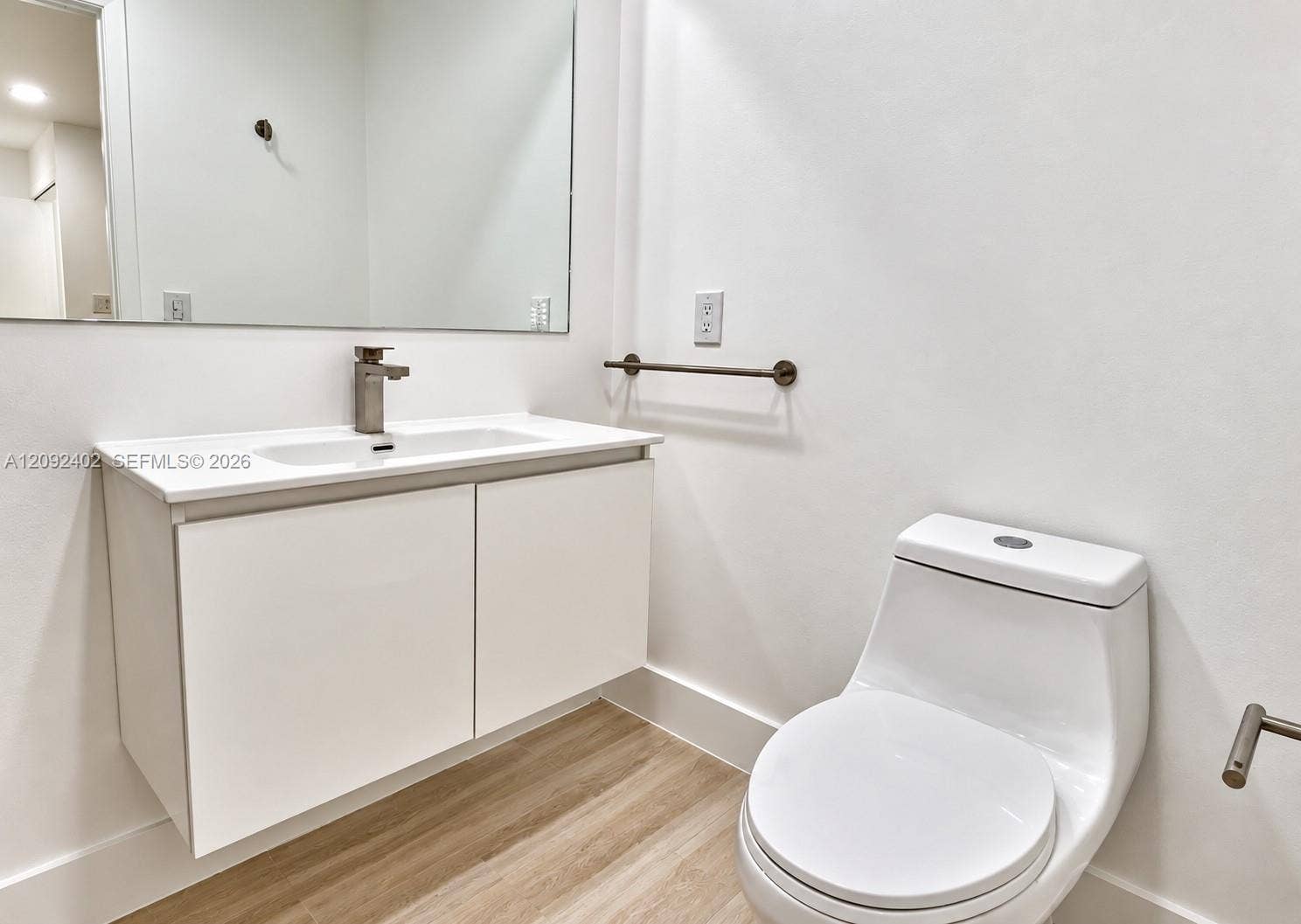 499 SE 13th Street, #7E, Fort Lauderdale, FL 33316 Floating vanity with a white countertop and integrated sink, wall-mounted faucet, expansive frameless mirror, one-piece dual-flush toilet, and wood-finish flooring
