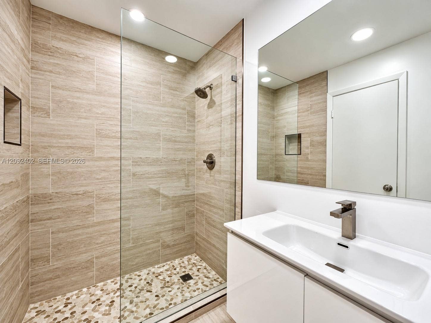 499 SE 13th Street, #7E, Fort Lauderdale, FL 33316 Walk-in shower featuring floor-to-ceiling textured tile, a river-stone floor, and a frameless glass enclosure, paired with a white vanity featuring a rectangular basin, stone countertop, and brushed metal fixtures