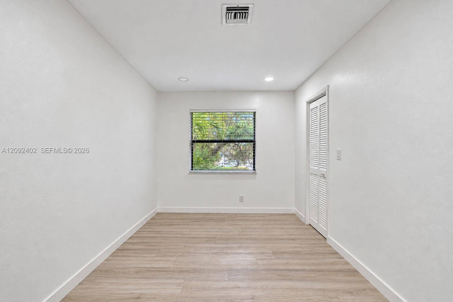 499 SE 13th Street, #7E, Fort Lauderdale, FL 33316 Neutral-toned room featuring wood-finish flooring, recessed lighting, and a window with horizontal blinds, complemented by a white louvered closet door