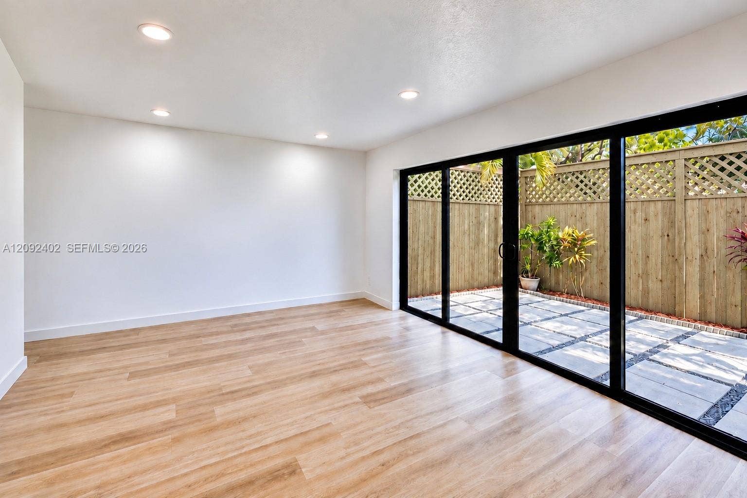 499 SE 13th Street, #7E, Fort Lauderdale, FL 33316 Interior space featuring wood-finish flooring, recessed lighting, and expansive black-framed sliding glass doors opening to a private patio with stone pavers and wooden lattice-topped fencing