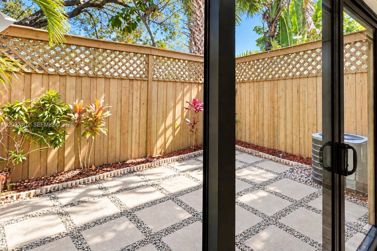 499 SE 13th Street, #7E, Fort Lauderdale, FL 33316 Private patio featuring concrete pavers with stone-filled grid detailing, enclosed by a wood privacy fence with lattice trim and landscaped border beds