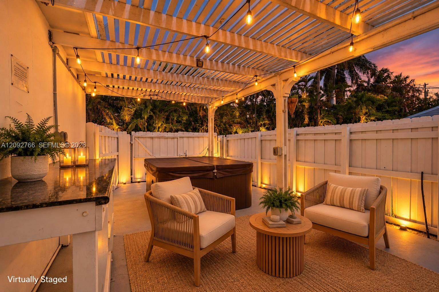 Covered pergola patio featuring integrated string lighting, built-in stone-top prep counter, and a private fenced perimeter