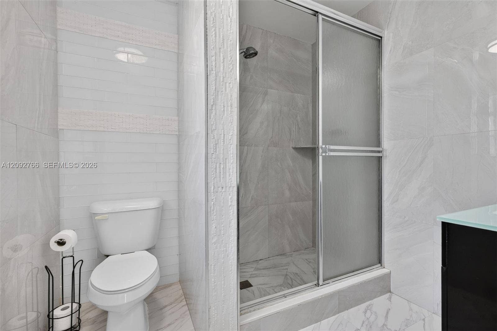 Bathroom featuring large-format gray tile shower surrounds, glass sliding shower enclosure, recessed shower shelving, and vertical white wall tile accents