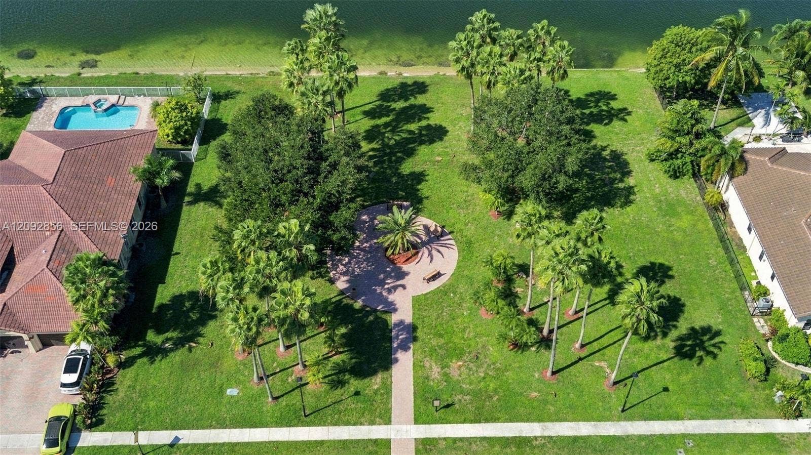 18919 SW 24th Street, #18919, Miramar, Miramar, FL 33029 Expansive waterfront lot featuring mature landscaping, a paved stone pathway, a circular hardscape patio, and an in-ground swimming pool