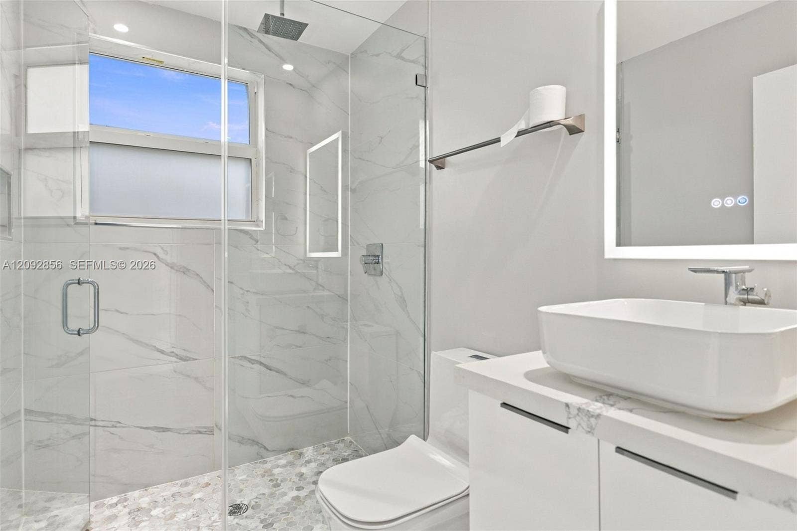 18919 SW 24th Street, #18919, Miramar, Miramar, FL 33029 2nd bathroom first floor - Cabana Bathroom featuring a glass-enclosed shower with floor-to-ceiling stone-patterned tile, a rainfall showerhead, a pebble-finish shower floor, a floating vanity with an integrated vessel sink, and an illuminated mirror