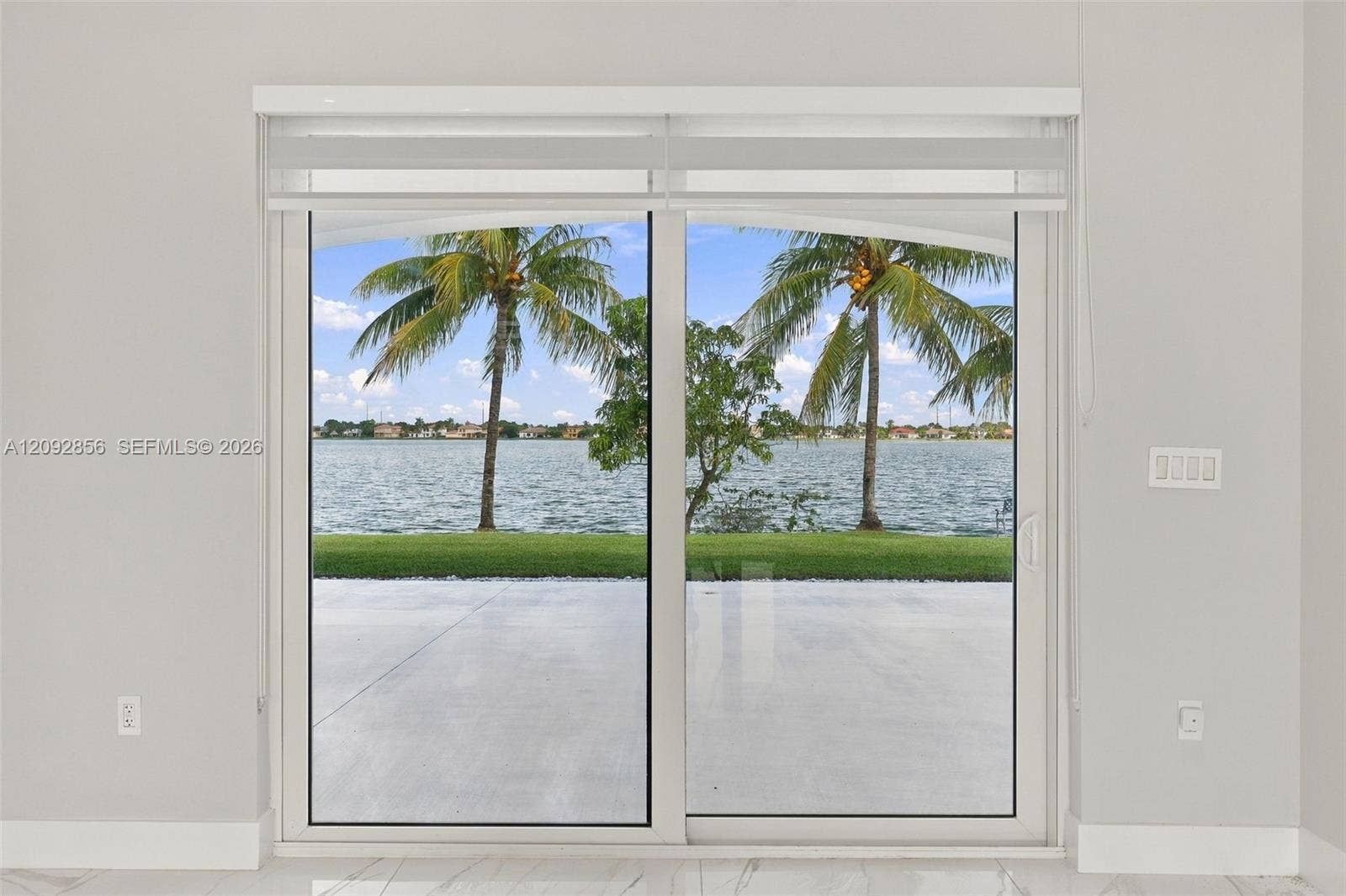 18919 SW 24th Street, #18919, Miramar, Miramar, FL 33029 Large sliding glass door featuring white framing, polished stone flooring, and expansive water frontage with palm trees