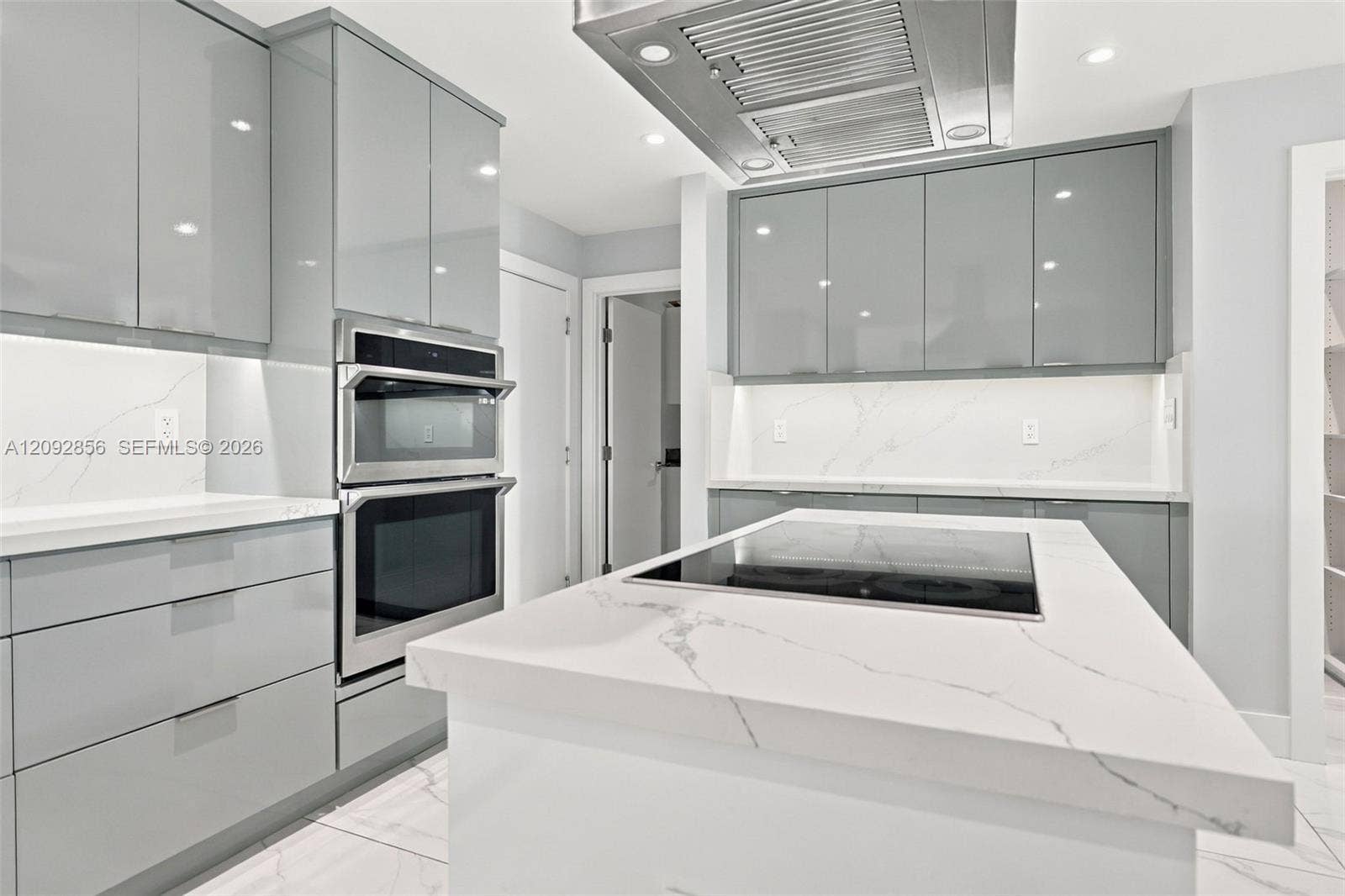 18919 SW 24th Street, #18919, Miramar, Miramar, FL 33029 Modern kitchen featuring high-gloss grey cabinetry, stone-surface countertops with waterfall edge, integrated induction cooktop, stainless steel built-in double oven, and industrial-style range hood