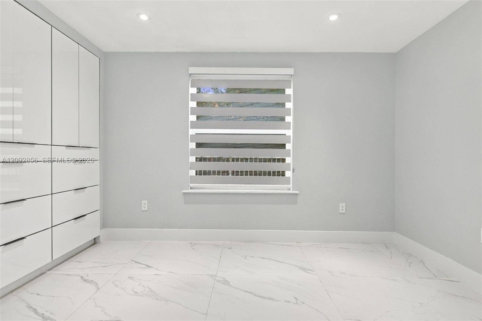 18919 SW 24th Street, #18919, Miramar, Miramar, FL 33029 2nd bedroom - 1st floor - Built-in floor-to-ceiling cabinetry with white high-gloss finish, large-format tile flooring with veining detail, recessed lighting, and a window featuring a dual-layer roller shade