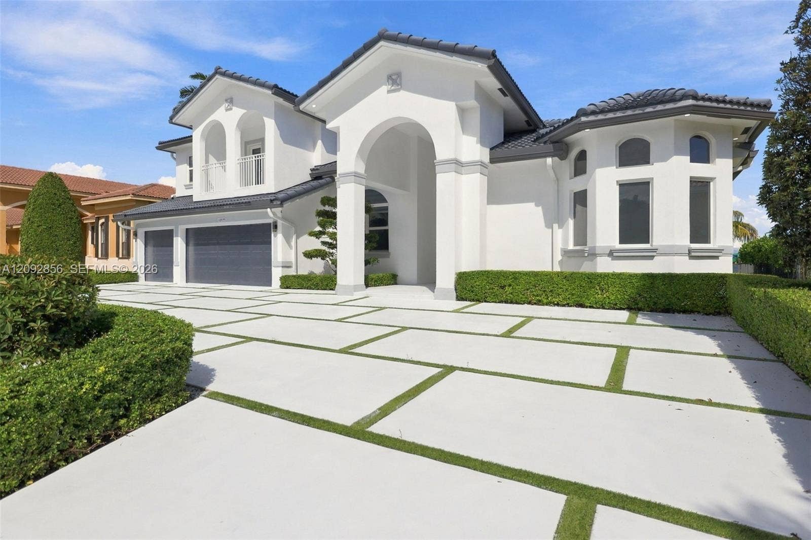 18919 SW 24th Street, #18919, Miramar, Miramar, FL 33029 Stucco exterior with a grand arched entryway, multi-car garage, tiled roof, and paver driveway with turf accents
