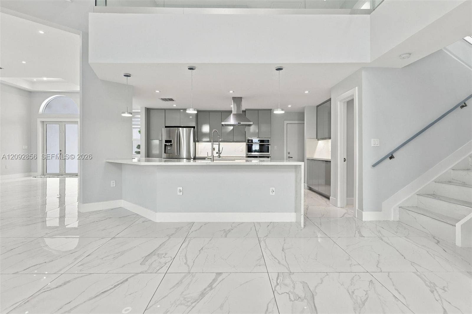 18919 SW 24th Street, #18919, Miramar, Miramar, FL 33029 Open-concept kitchen featuring large-format tile flooring, gray gloss cabinetry, a stainless steel range hood, quartz countertops, and a glass-paneled staircase railing