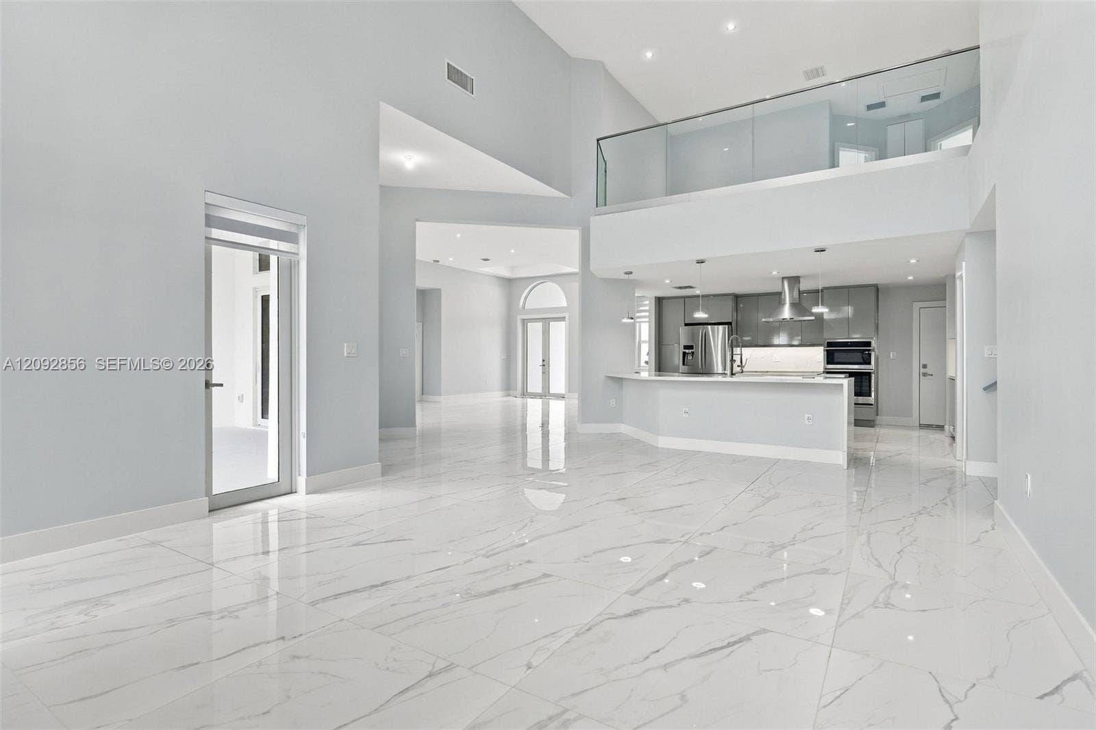 18919 SW 24th Street, #18919, Miramar, Miramar, FL 33029 Open-concept interior with vaulted ceilings, large-format veined tile flooring, glass-panel balcony railing, stainless steel built-in appliances, and recessed lighting
