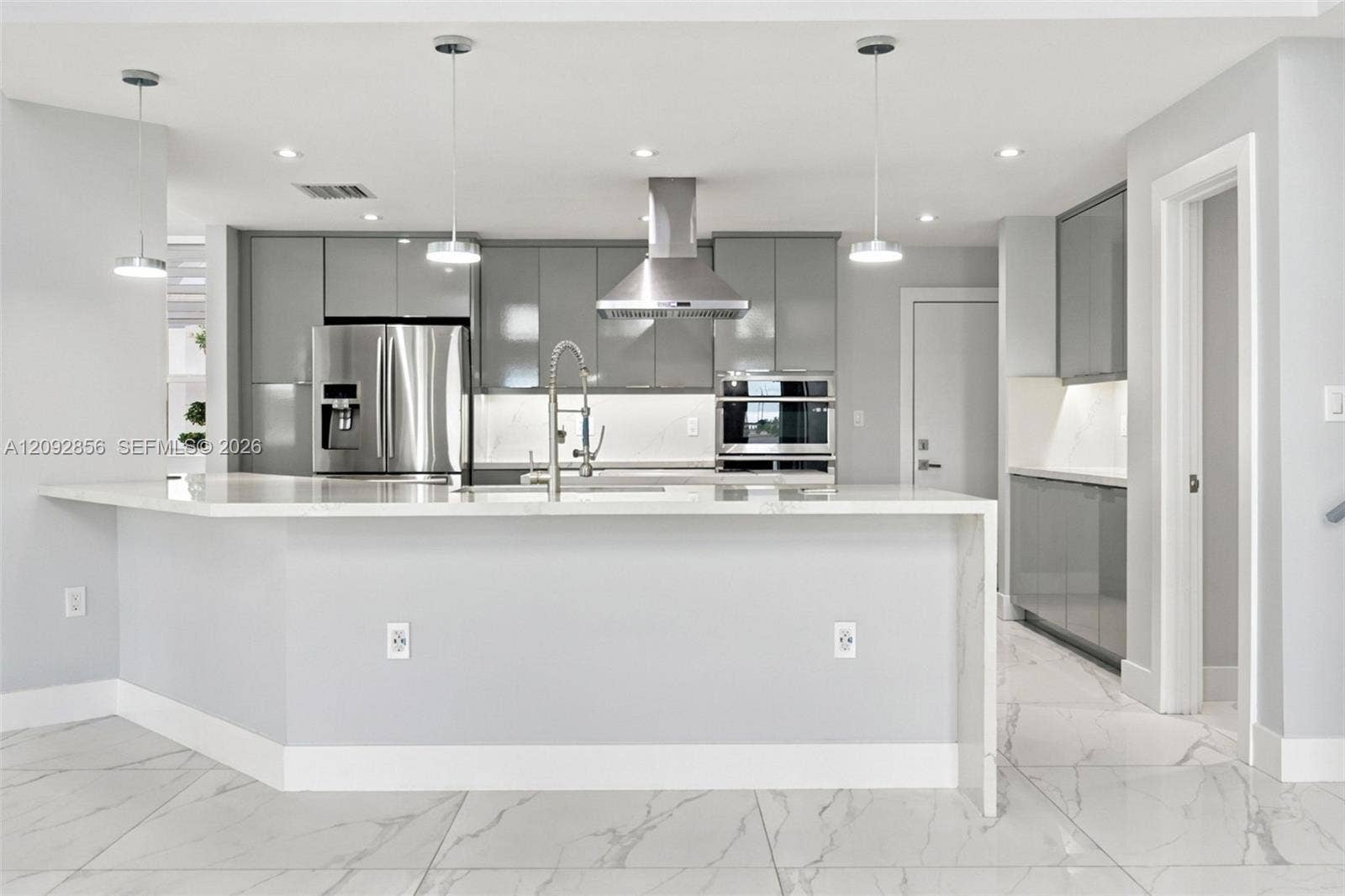 18919 SW 24th Street, #18919, Miramar, Miramar, FL 33029 Kitchen featuring high-gloss cabinetry, stone-surface waterfall island, stainless steel appliances, built-in range hood, and large-format tile flooring