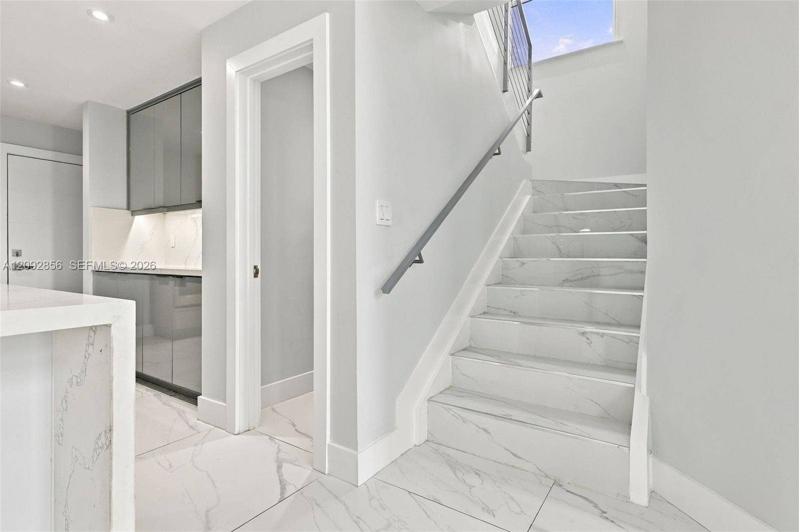 18919 SW 24th Street, #18919, Miramar, Miramar, FL 33029 Staircase featuring stone-finish treads, a metal handrail, and white-finish wall accents, paired with nearby cabinetry featuring sleek hardware and integrated lighting