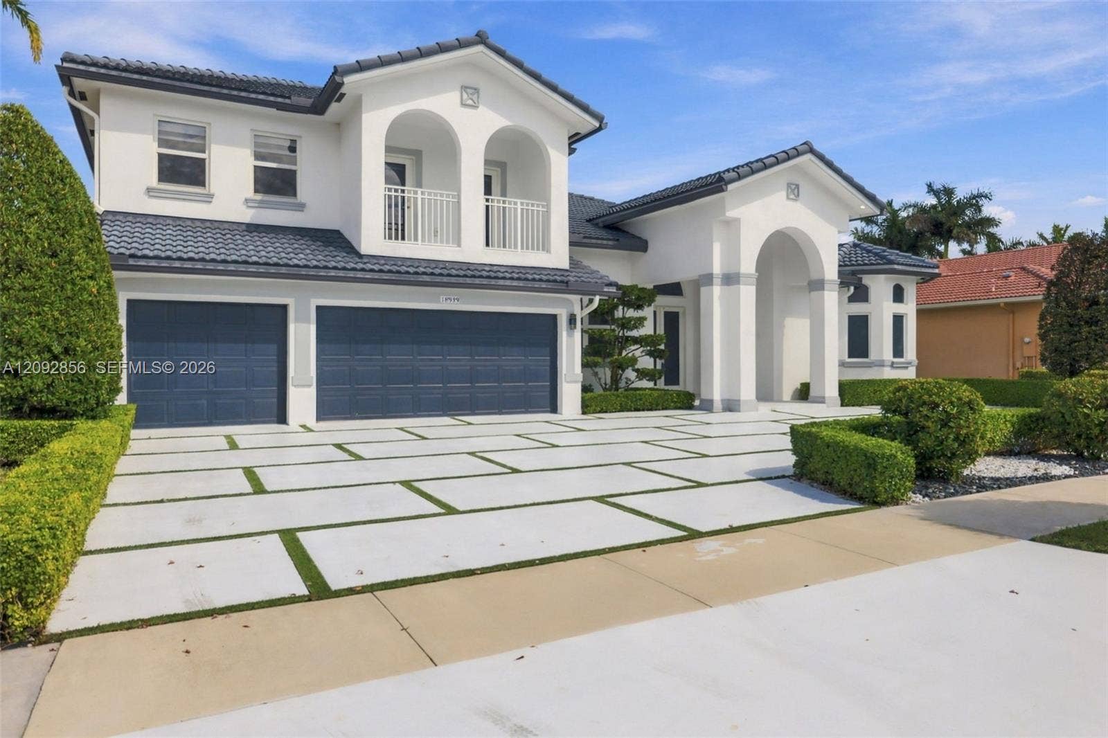 18919 SW 24th Street, #18919, Miramar, Miramar, FL 33029 Mediterranean-style exterior featuring a tile roof, stucco finish, three-car garage, covered entryway with arched columns, and a paved driveway with integrated lawn grid