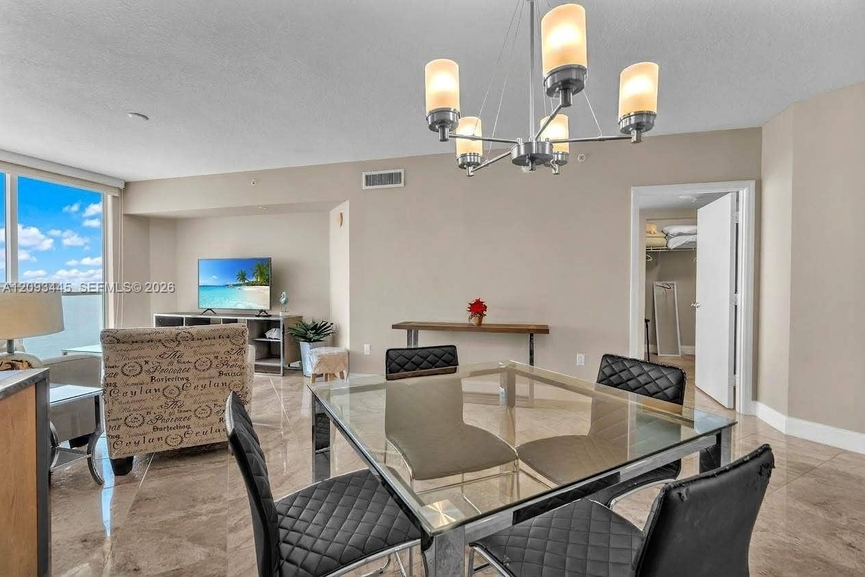 Expansive open-concept living area featuring a contemporary chandelier, large format tile flooring, and floor-to-ceiling windows