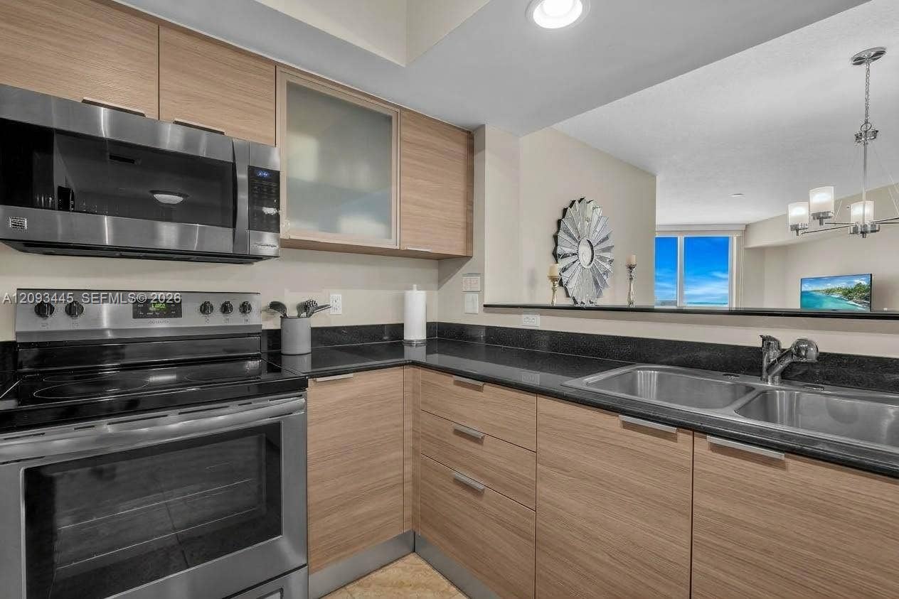 Kitchen cabinets modernized by A.I Kitchen featuring dark wood-finish cabinetry, black countertops, stainless steel appliances, and recessed lighting