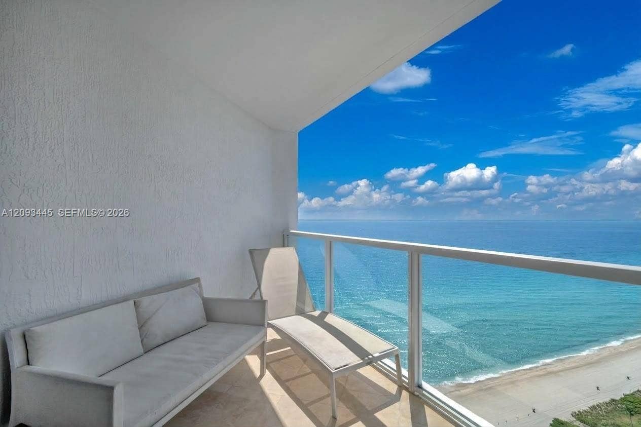 Balcony featuring glass panel railings, textured white walls, and an ocean backdrop