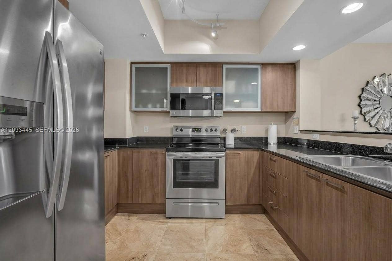 Kitchen cabinets modernized by A.I Stainless steel appliances, wood-finish cabinetry, dark countertops, tile flooring, and recessed lighting-