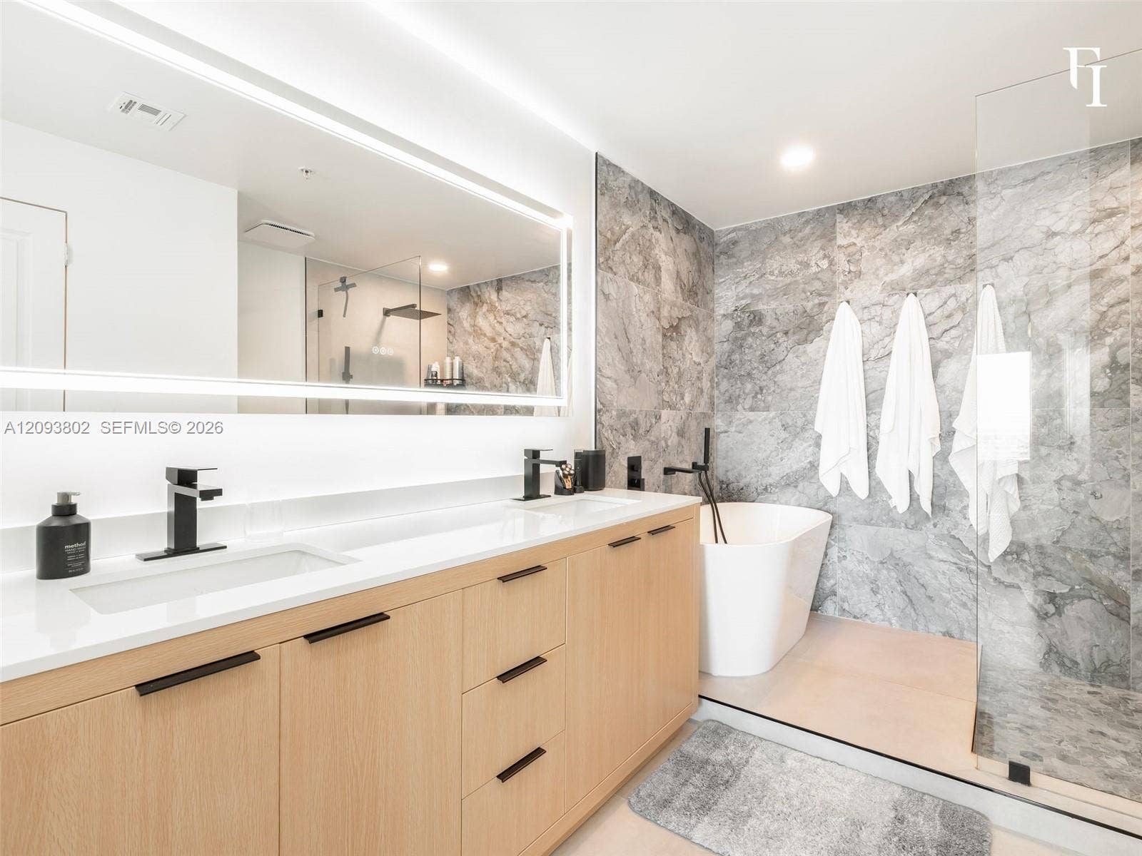 7910 Harbor Island Drive, #909, North Bay Village, North Bay Village, FL 33141 Floating wood-finish vanity with dual integrated sinks and quartz countertops, oversized backlit mirror, freestanding soaking tub, and stone-tiled shower enclosure with glass surround