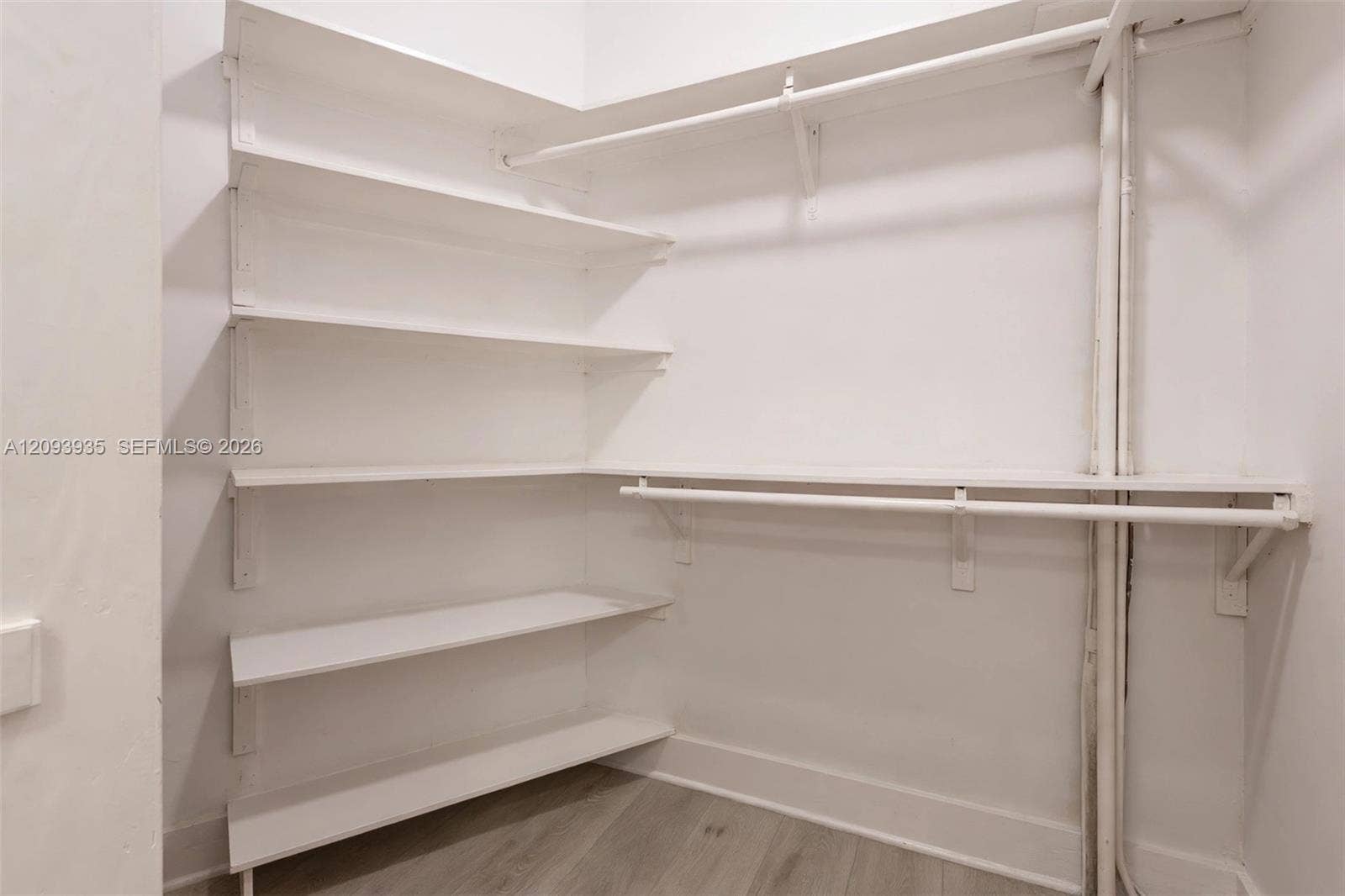 Storage area featuring white built-in shelving, dual-level hanging rods, and wood-finish flooring