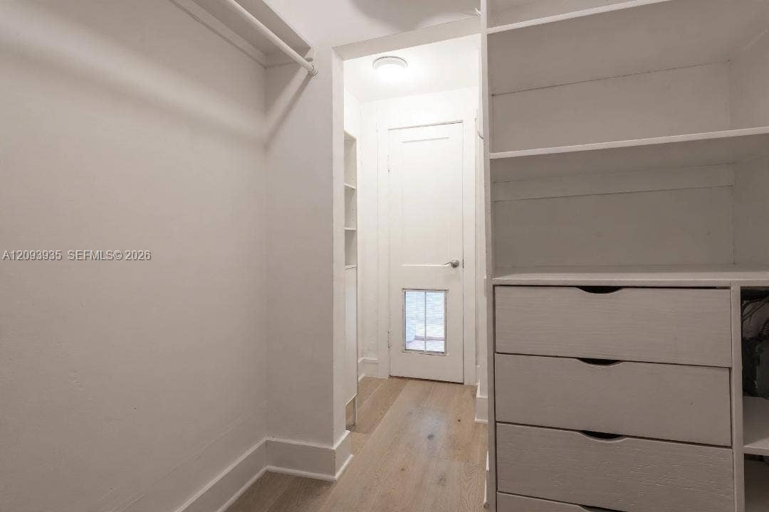 Walk-in closet featuring white built-in shelving, integrated dresser drawers, hanging rods, and wood-finish flooring