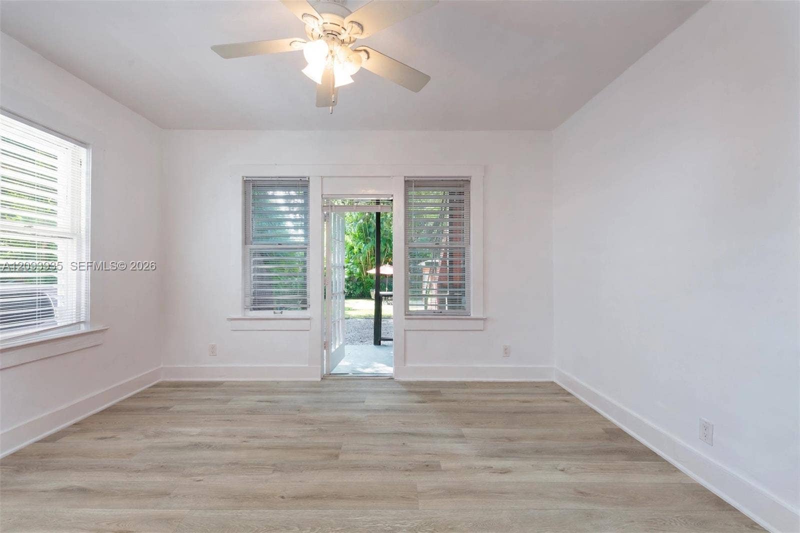 Interior space featuring wood-finish flooring, white walls, shutter-style window coverings, a ceiling-mounted light fixture with a fan, and an exterior door