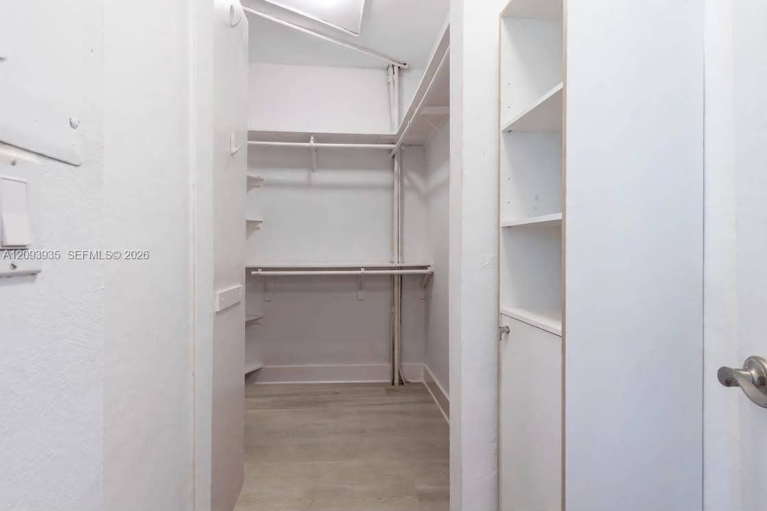Walk-in closet featuring wood-finish flooring, multi-tier hanging rods, and built-in vertical shelving