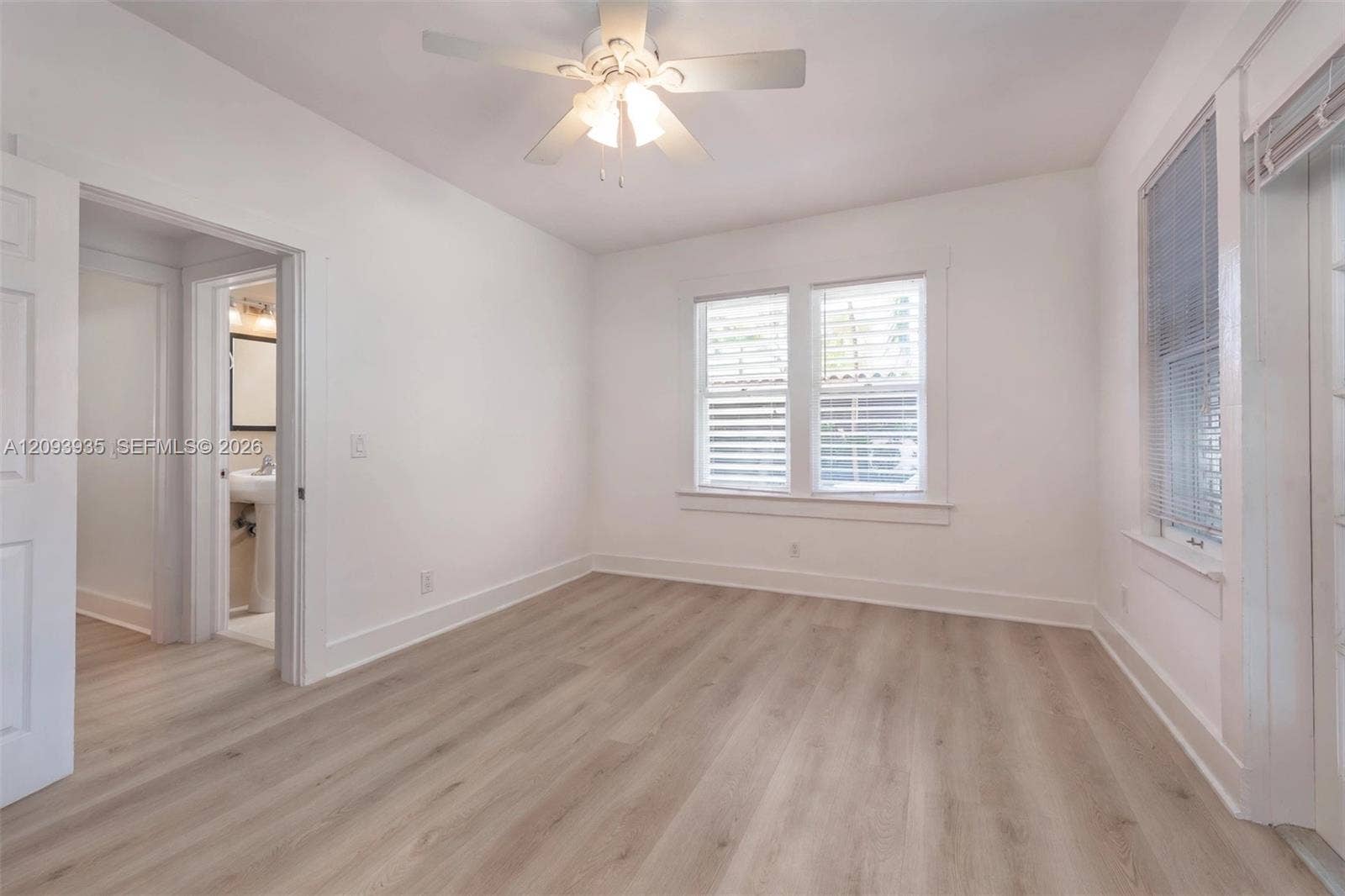 Interior space featuring wood-finish flooring, dual windows with blinds, and a white ceiling fan with integrated lighting