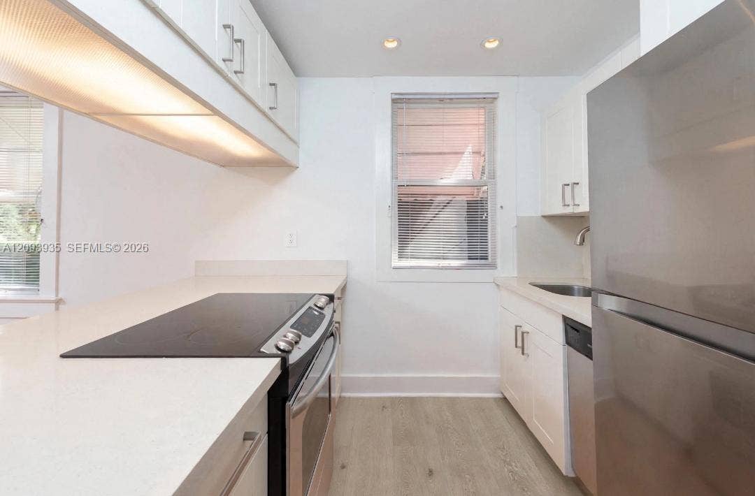 Kitchen featuring white cabinetry, solid surface countertops, stainless steel appliances, and wood-finish flooring