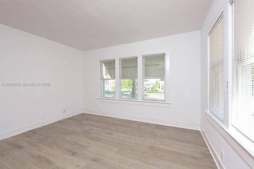 Neutral interior featuring wood-finish flooring, white walls, and multiple windows with horizontal blinds