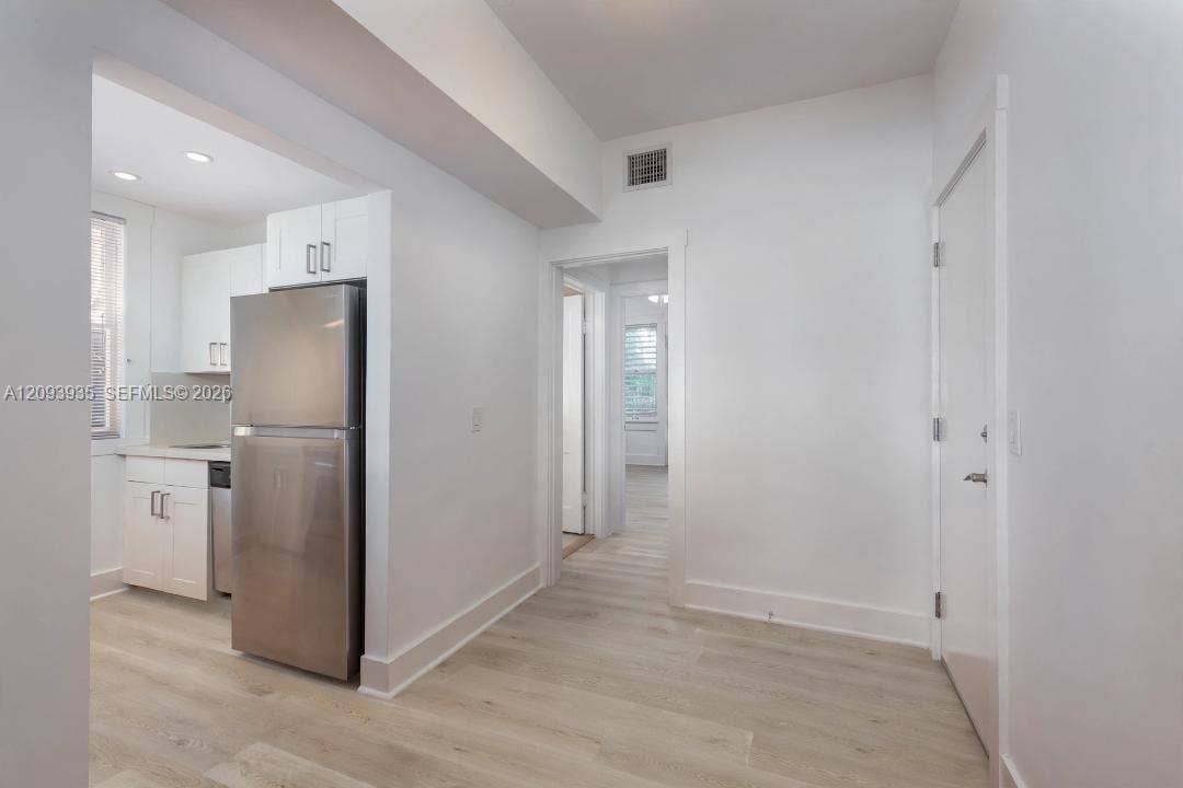Interior featuring wood-finish flooring, white cabinetry with silver-tone hardware, and a stainless steel refrigerator