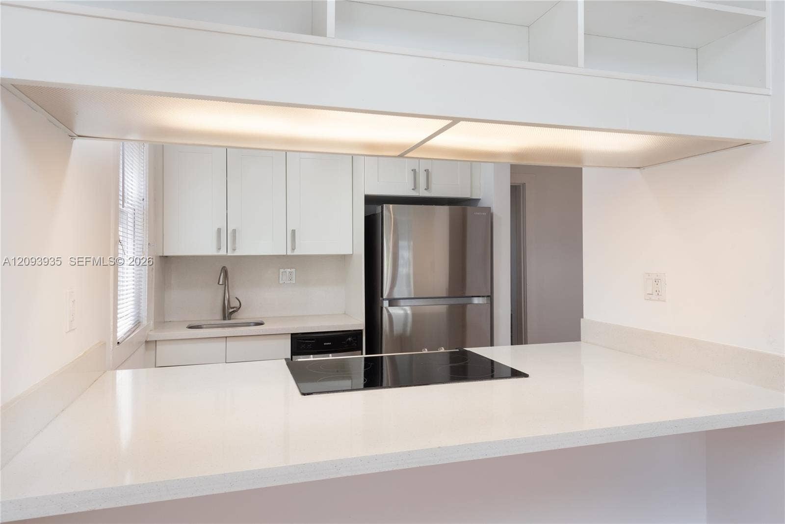 Kitchen featuring white cabinetry, solid-surface countertops, built-in cooktop, stainless steel refrigerator, and integrated under-cabinet lighting