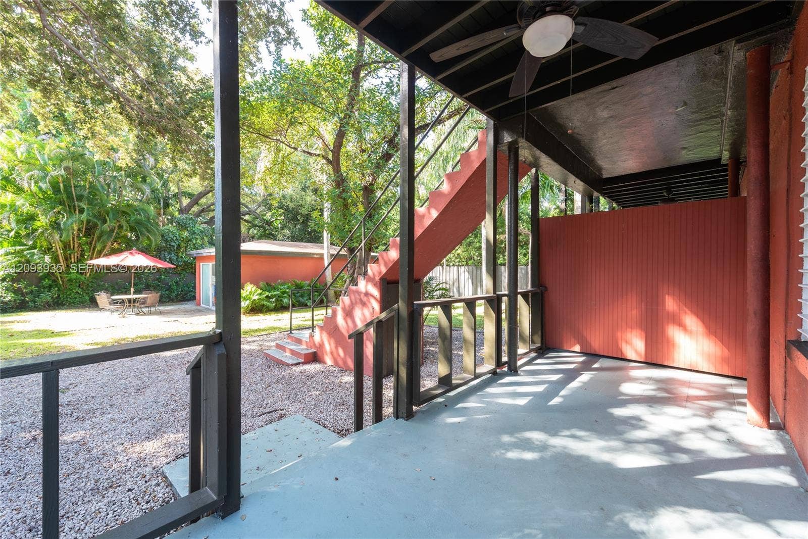 Covered patio featuring a ceiling fan, exterior metal staircase, painted concrete flooring, and privacy screening