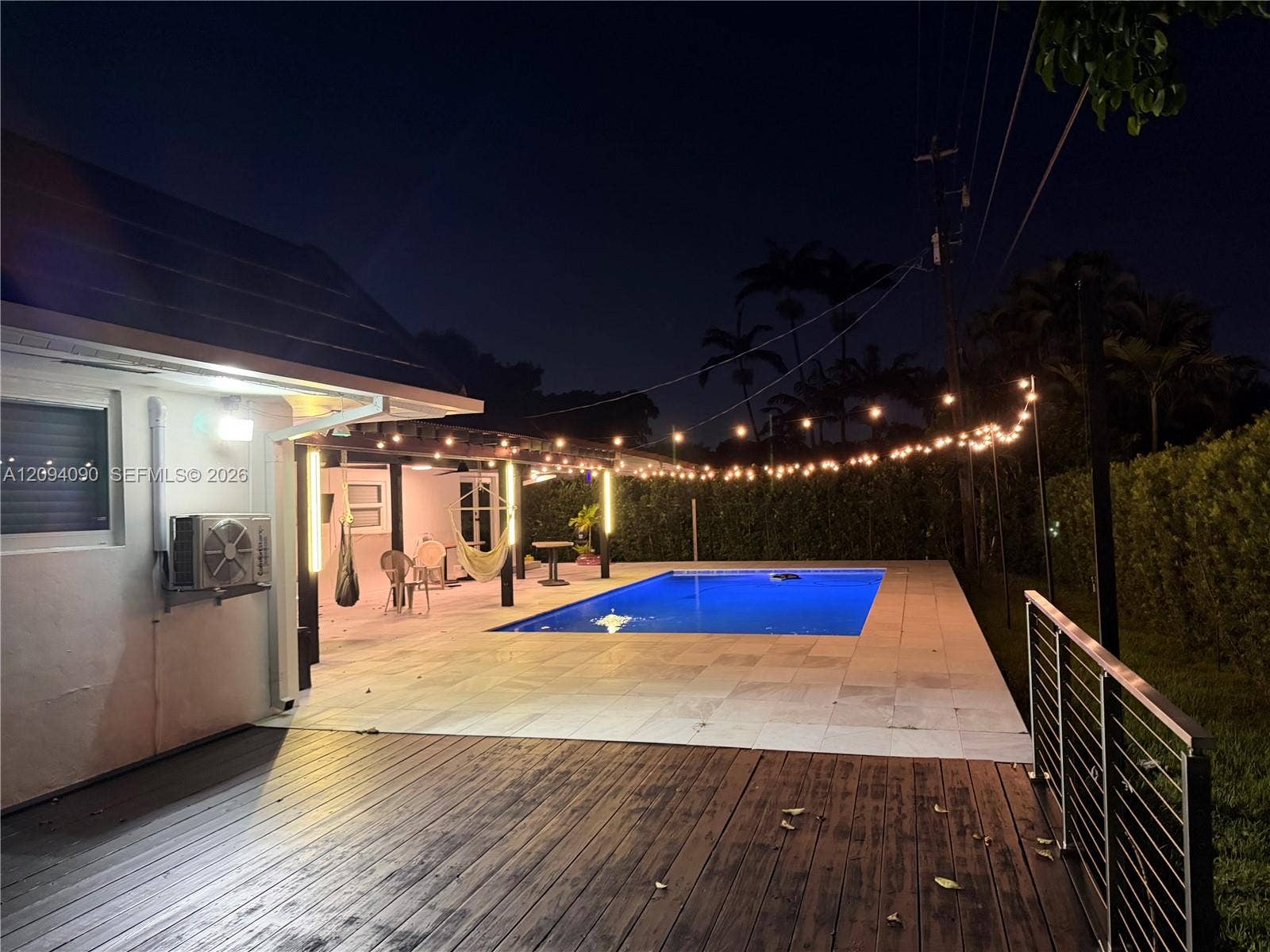 2215 NE 204th Street, Miami, FL 33180 Expansive outdoor living area featuring a rectangular pool, wood-plank decking, and a covered patio with string lighting