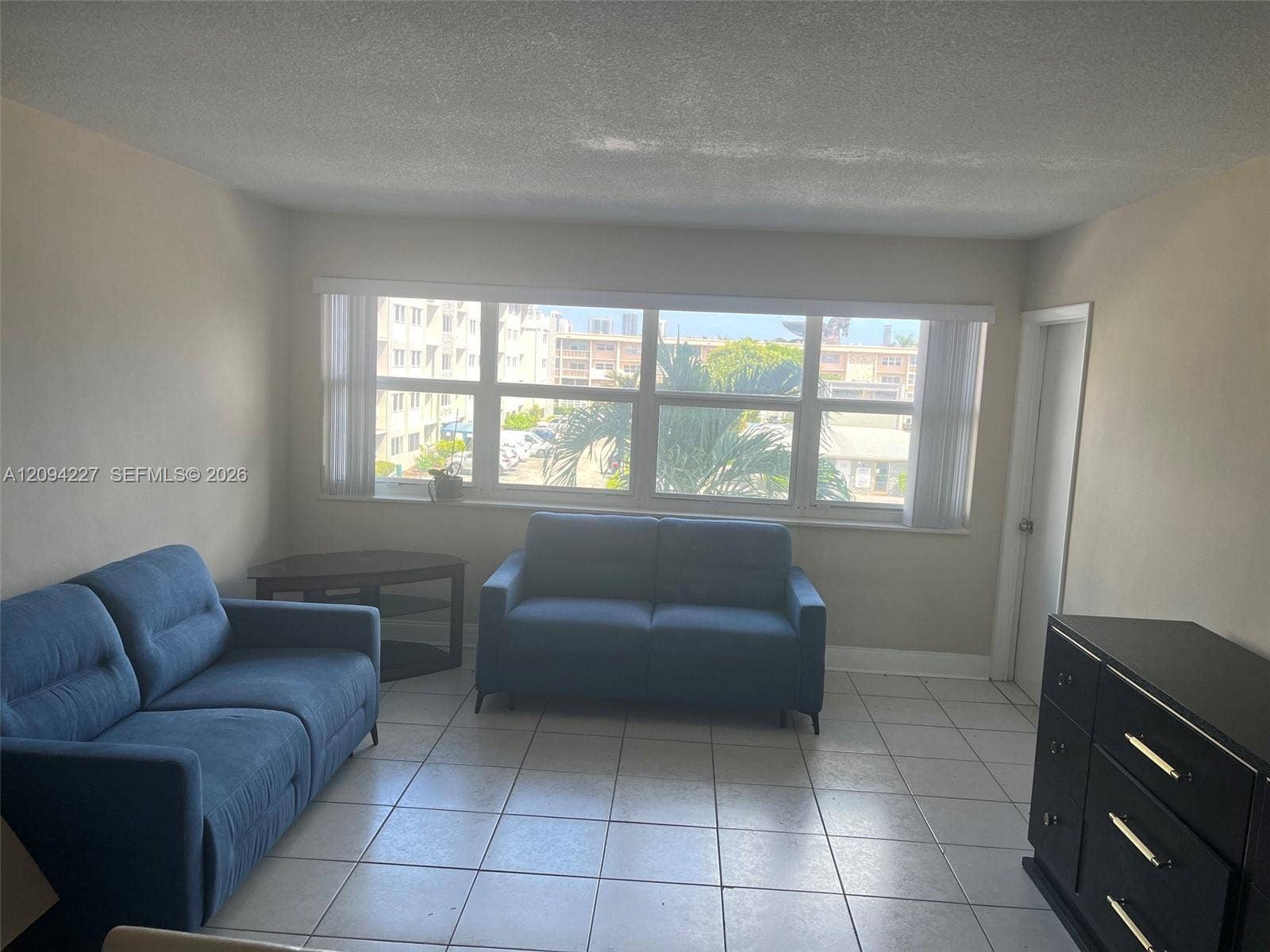 Neutral interior featuring light-colored floor tiling, large multi-pane windows with vertical blinds, and a solid-core interior door
