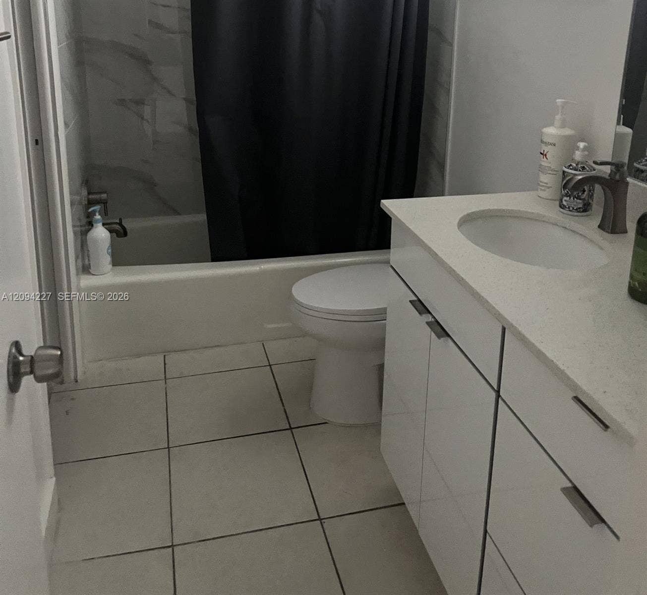White vanity featuring a composite countertop with an integrated basin, brushed-metal hardware, tile flooring, and a tub-shower combination with surround tile