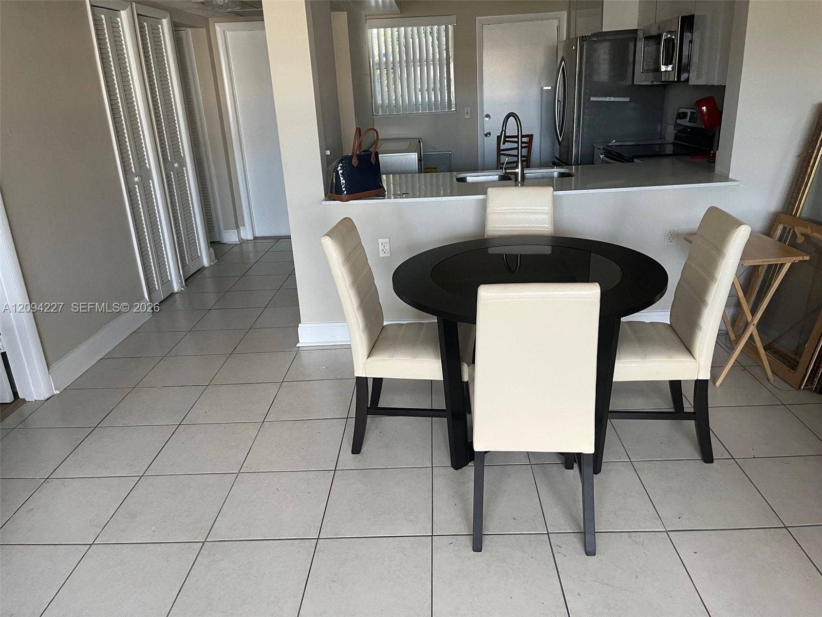 Kitchen featuring a pass-through breakfast bar with a stone-surface countertop, stainless steel refrigerator, built-in microwave, double-basin sink, and tile flooring