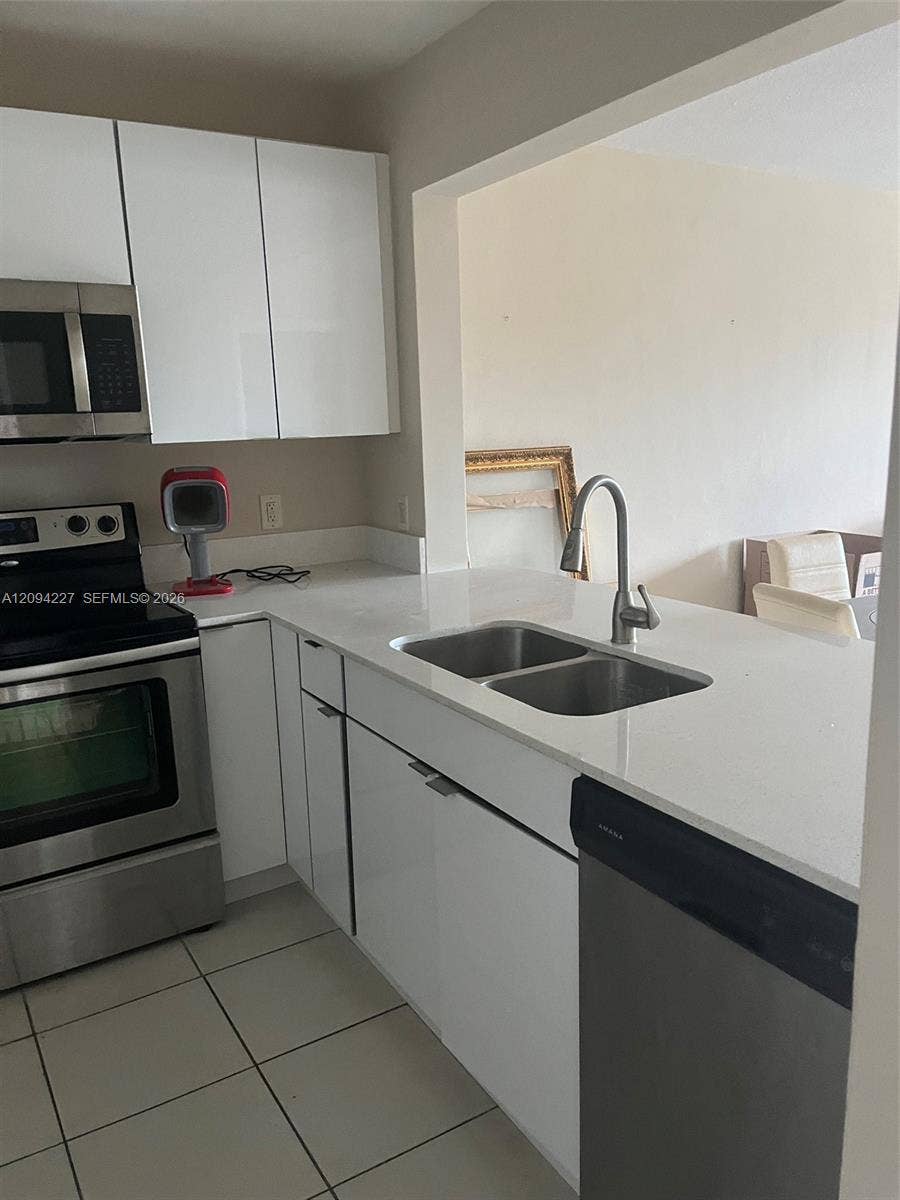 Kitchen featuring white high-gloss cabinetry, stone-finish countertops, stainless steel appliances, dual-basin sink with arched faucet, and tiled flooring
