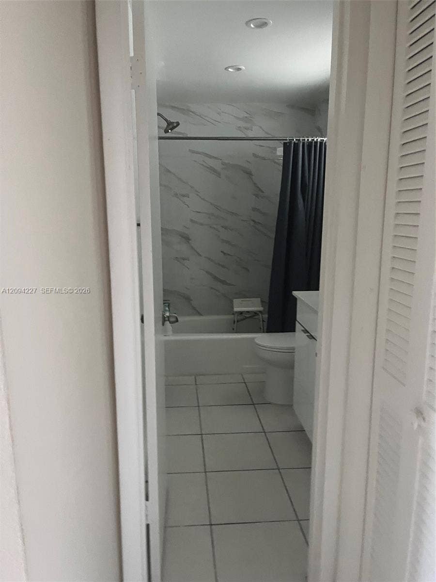 Bathroom featuring large-format floor tiling, a white vanity cabinet, recessed ceiling lighting, and a bathtub surround with full-height decorative wall tile