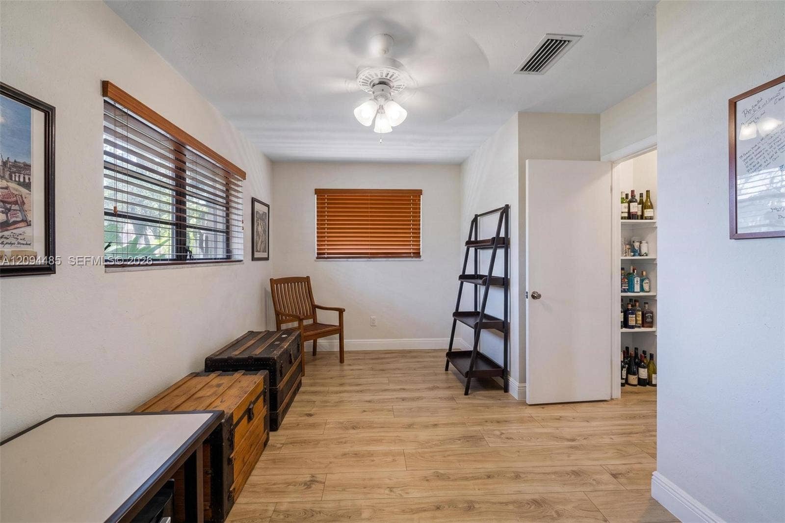 Room featuring wood-finish flooring, dual windows with horizontal blinds, a ceiling fan with integrated lighting, and a reach-in pantry