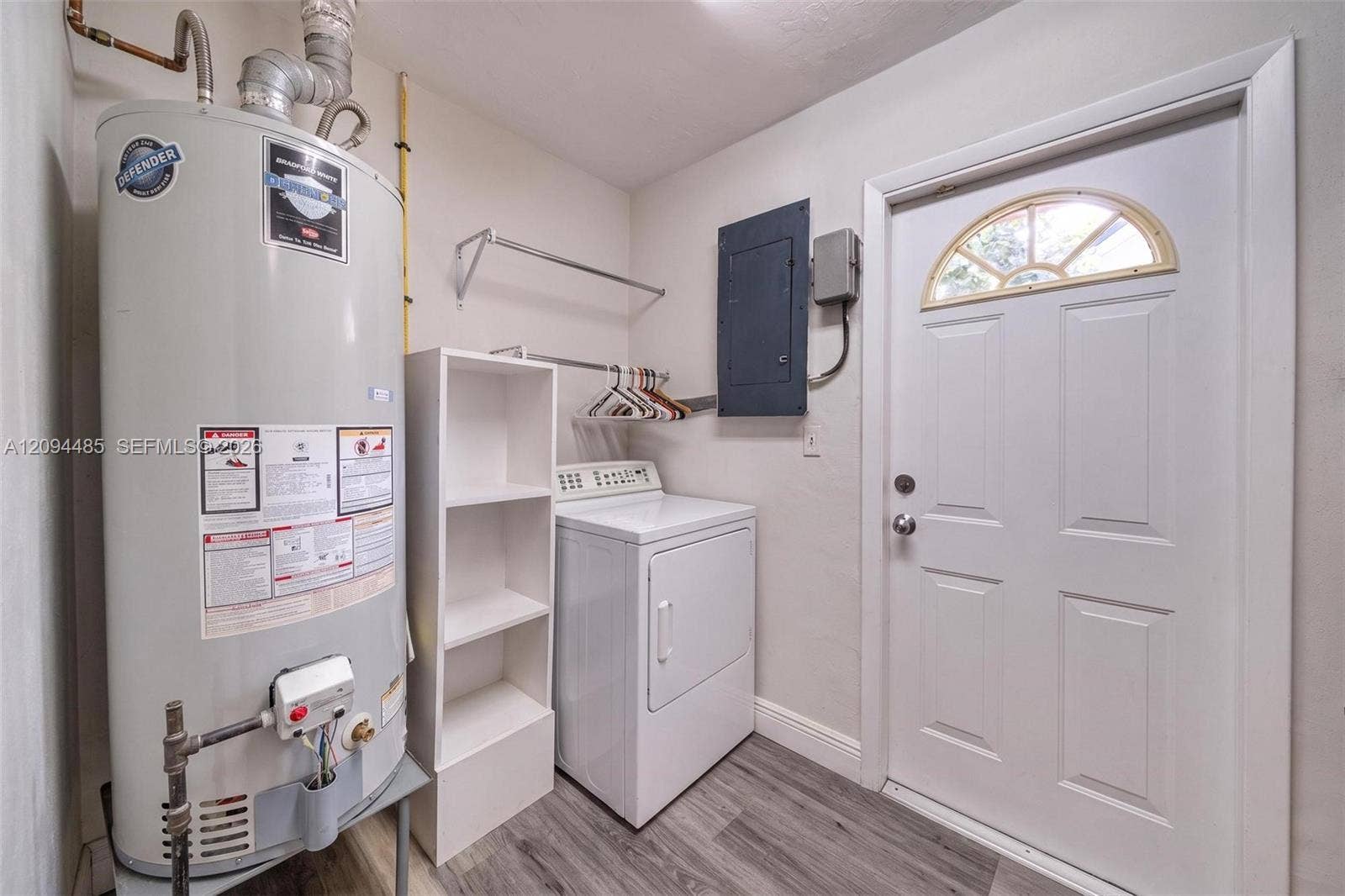 Utility area featuring wood-finish flooring, a white metal exterior door with a semi-circular transom window, and white built-in shelving