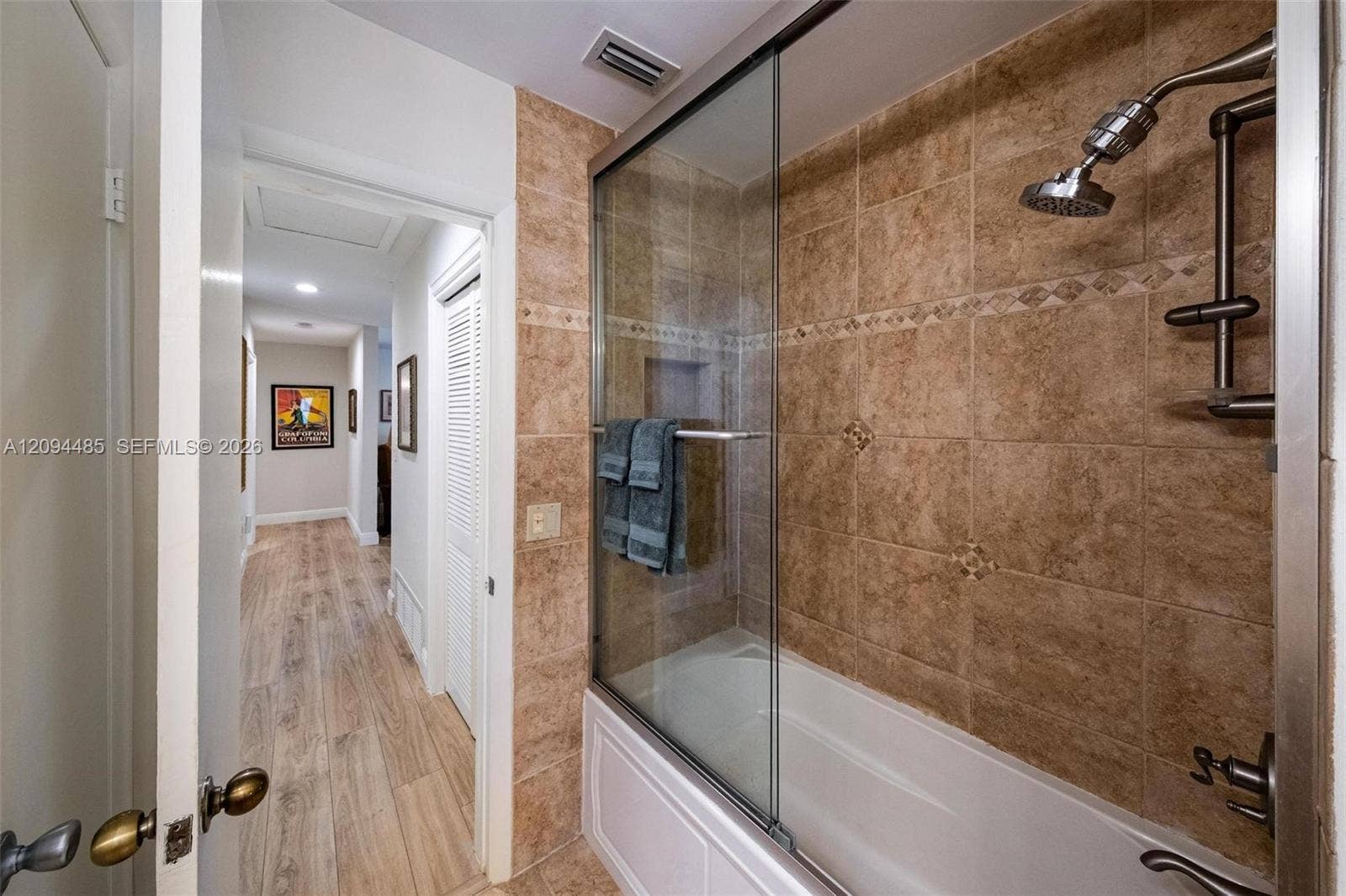 Shower-tub combination featuring floor-to-ceiling tile surround with decorative inlay, glass sliding shower door, recessed wall niche, and metal hardware