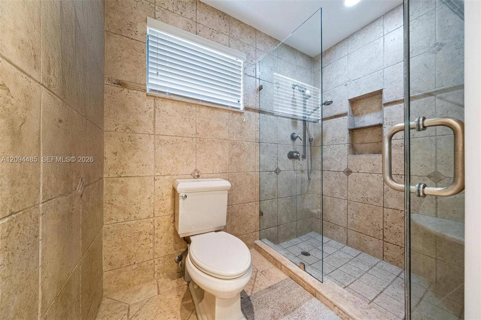 Walk-in shower featuring glass enclosure, built-in recessed shelving, wall-mounted shower head, and tile surround with integrated tile flooring