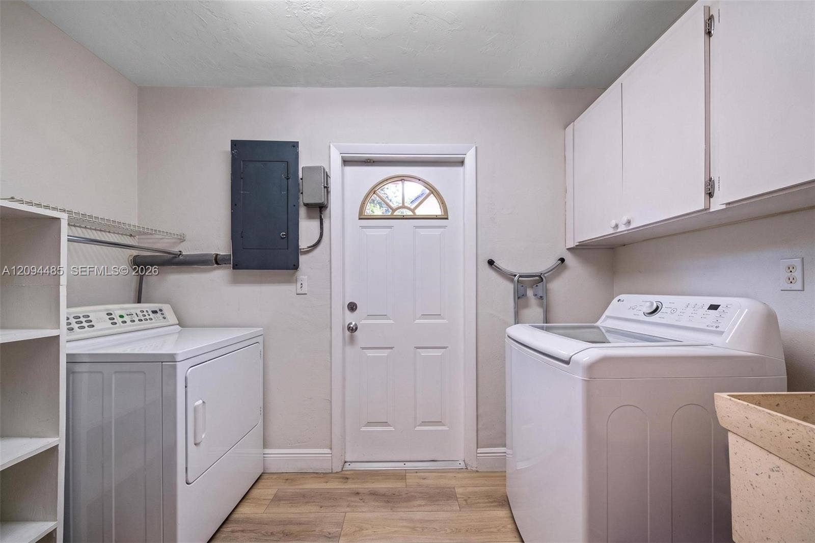 Laundry area featuring wood-finish flooring, white upper wall-mounted cabinetry, integrated shelving, and a utility sink