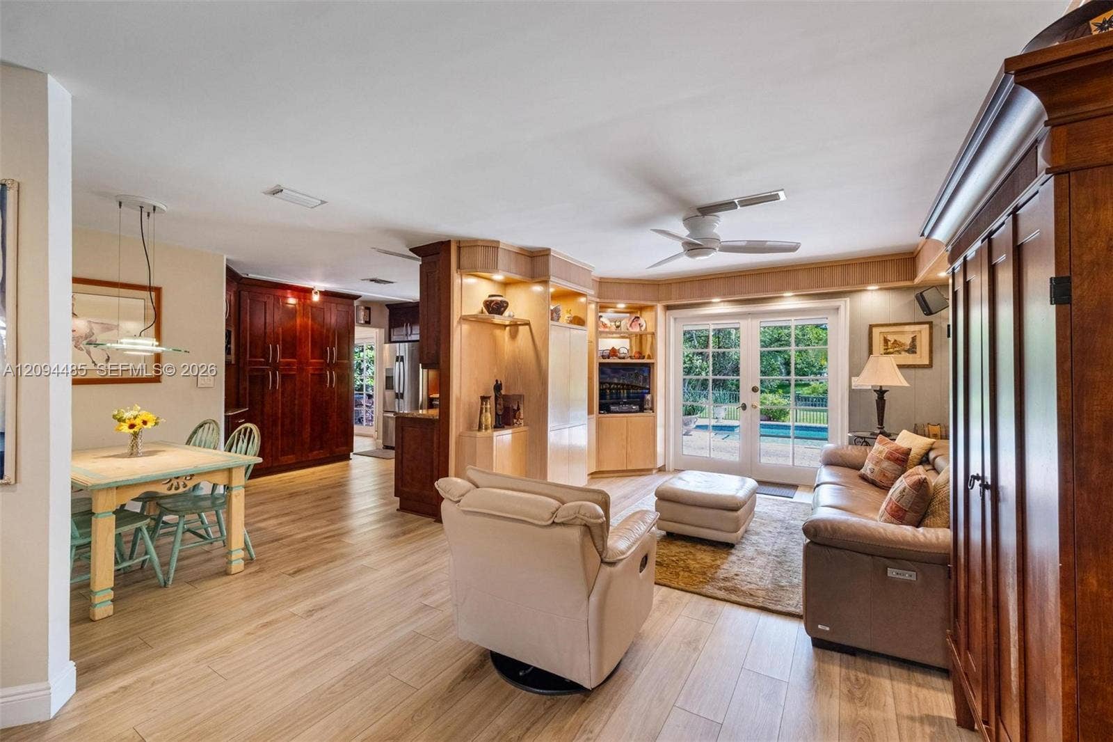 Open-concept interior featuring wood-finish flooring, custom built-in cabinetry with recessed lighting, dark wood pantry doors, and French doors
