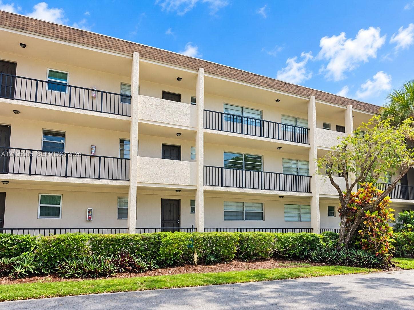 Multi-story exterior featuring a stucco facade, horizontal railings, stacked balconies, and low-maintenance landscaping