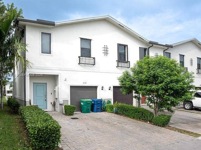 Two-story stucco exterior featuring a paver driveway, two-car garage, upper-level window boxes, and exterior wall-mounted decorative accents